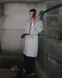 Man wearing beige trench coat holding a vintage corded telephone handset in Sydney, photographed by Will Stokoe.