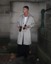 Man wearing a beige trench coat over a white shirt and black trousers holding two vintage telephone handsets