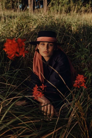 Portrait of woman wearing a hat in a grassy field with red flowers. The light is soft and golden, and the background is blurred.