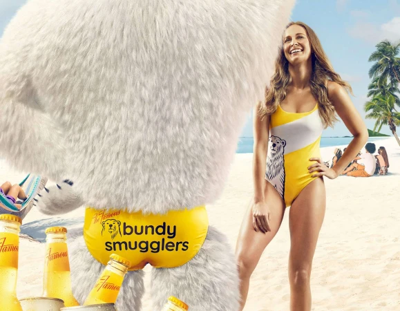 A woman in a swimsuit stands on a beach next to a person in a polar bear costume, with beer bottles on the sandy ground.