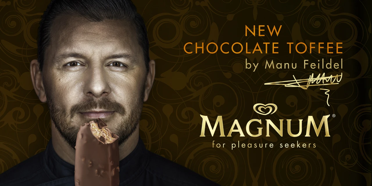 Close-up of a male model with a bite taken out of a Magnum chocolate toffee ice cream bar, in front of a swirly brown background.