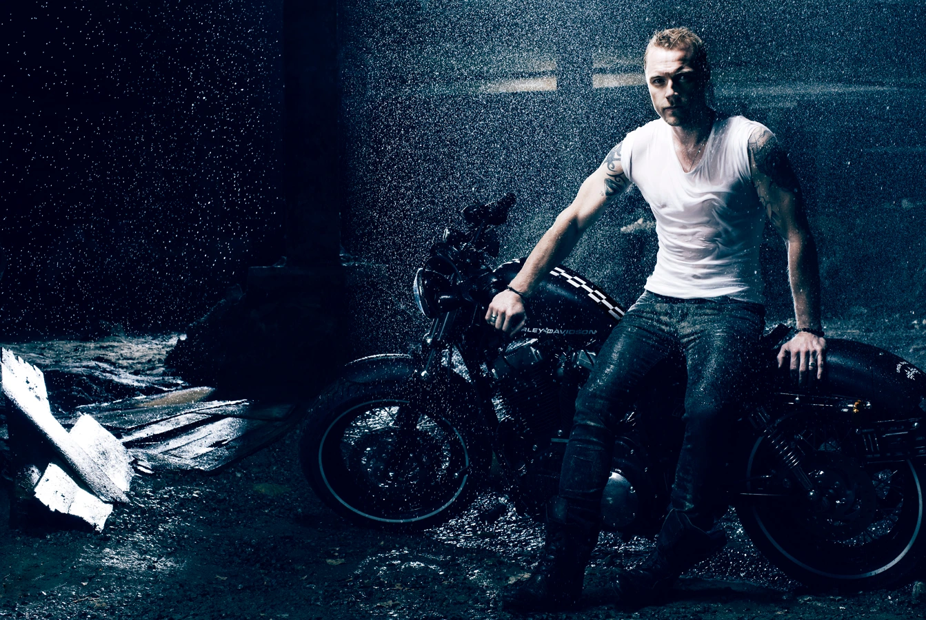 Man sitting on a black motorcycle in the rain under dramatic lighting by Richard Freeman