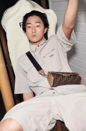 East Asian man in grey utility shirt and shorts with crossbody monogram bag by makeup artist Ava Belle