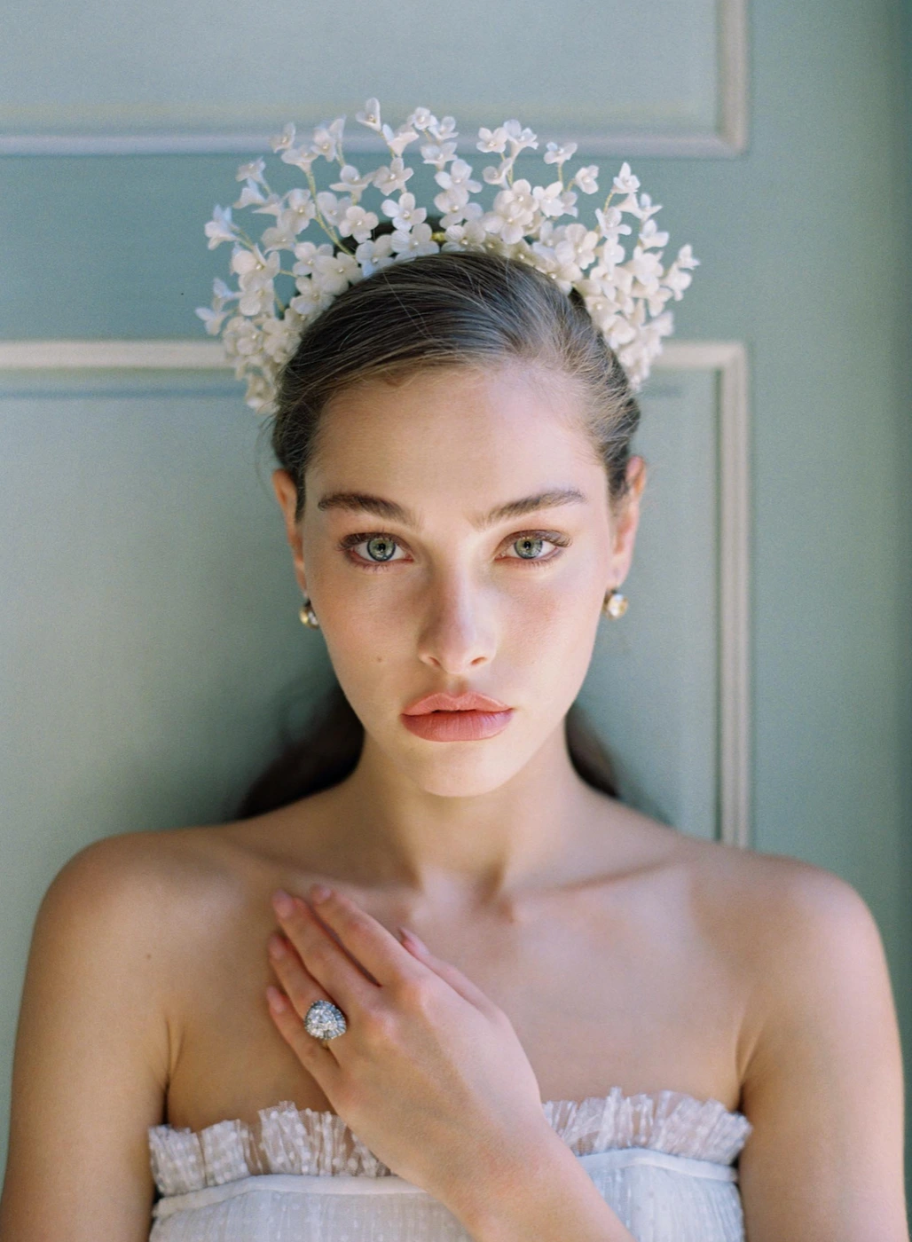 Model wearing a white floral headpiece and white ruffled dress against a teal panelled wall by makeup artist Ava Belle