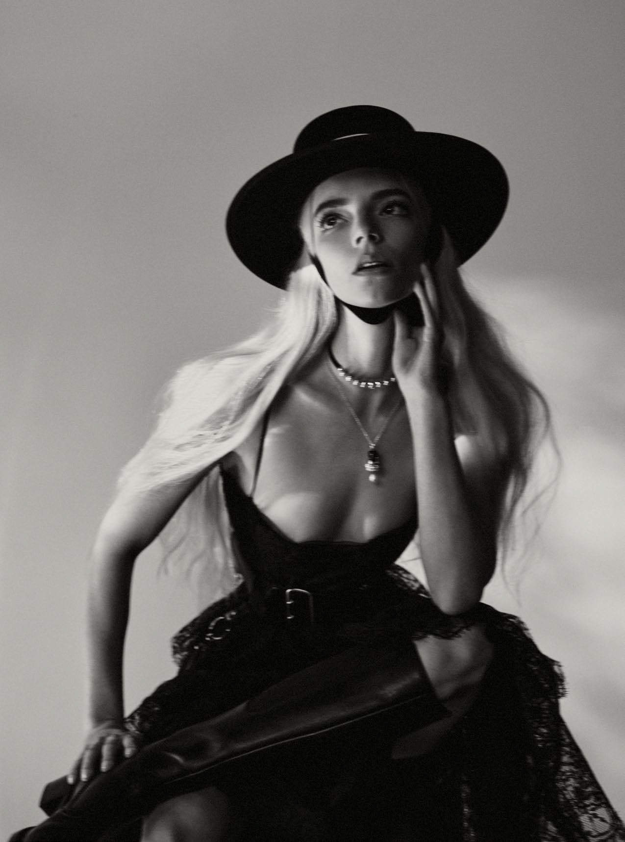 Black and white portrait of a woman with blond hair wearing a black hat, necklace, and black lace dress, posing in a photo studio.
