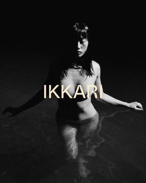Monochrome portrait of a woman standing in water, her upper body and face partially shadowed, with the word 'IKKARI' overlaid.