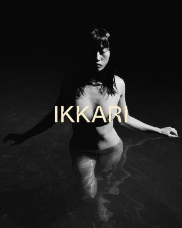 Monochrome portrait of a woman standing in water, her upper body and face partially shadowed, with the word 'IKKARI' overlaid.