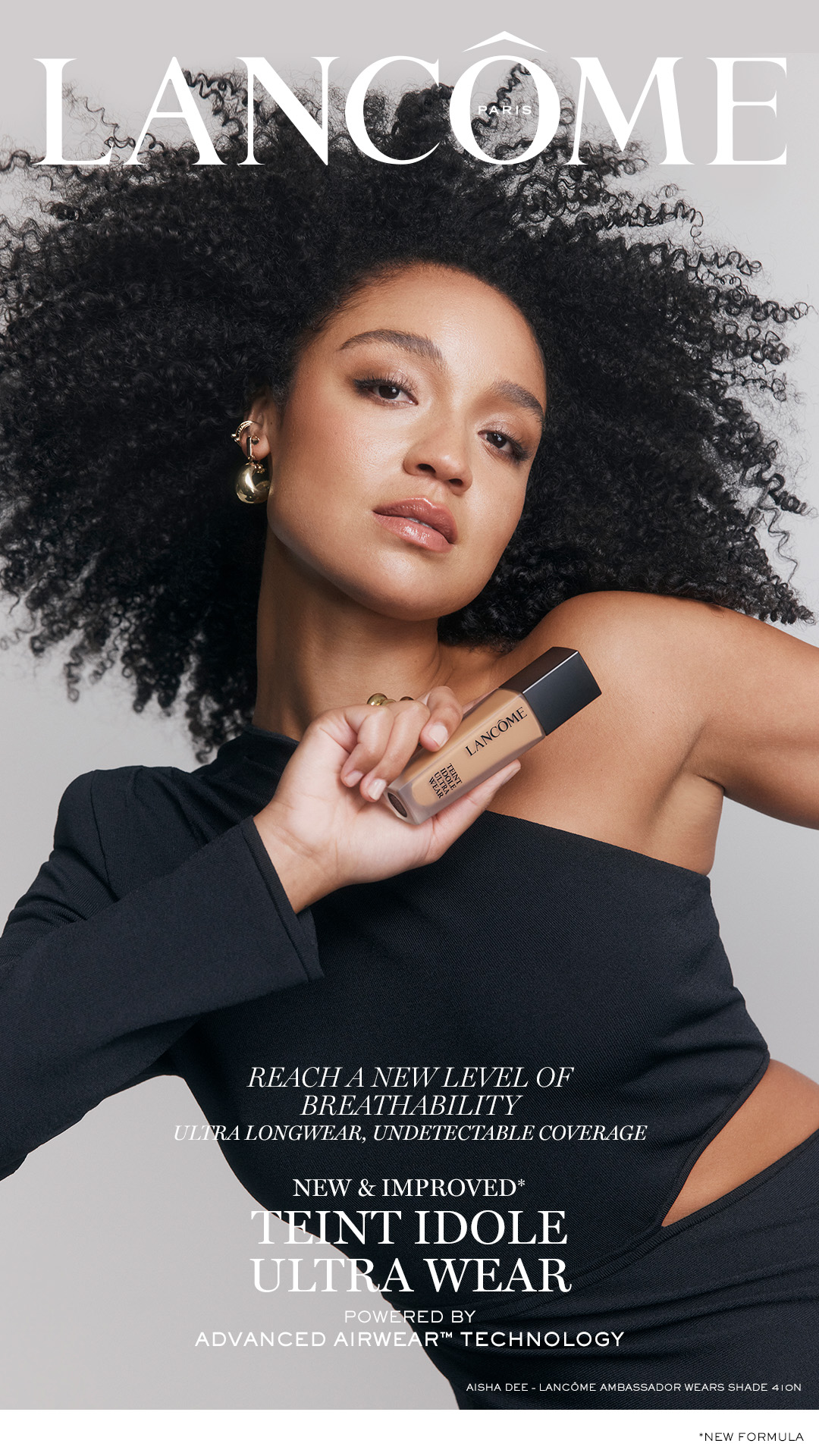 Cosmetics advertisement for Lancome featuring a woman with curly hair holding a bottle of Teint Idole Ultra Wear foundation.