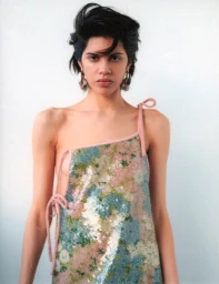 Model with dark styled hair wearing a sequined patterned top against a white wall in Sydney by Clara Leonard