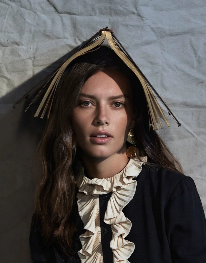 Woman wearing an open book on her head like a hat against a textured wall