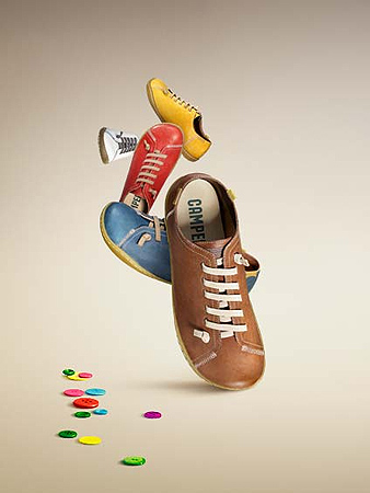 Colorful Camper shoes in a dynamic mid-air arrangement with scattered buttons against a soft gradient background. Eye-catching product shot.