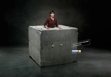 A woman emerging from inside a large solid concrete cube block in a dark studio setting photographed by Garrigosa.