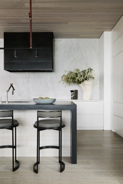Contemporary kitchen interior featuring a breakfast bar with two bar stools, a marble backsplash, and a black range hood.