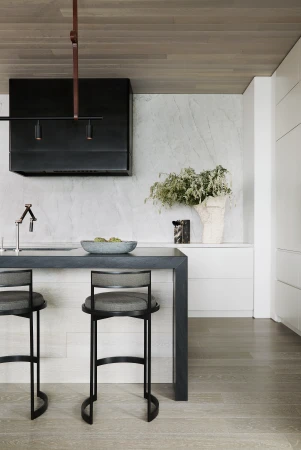 Contemporary kitchen interior featuring a breakfast bar with two bar stools, a marble backsplash, and a black range hood.
