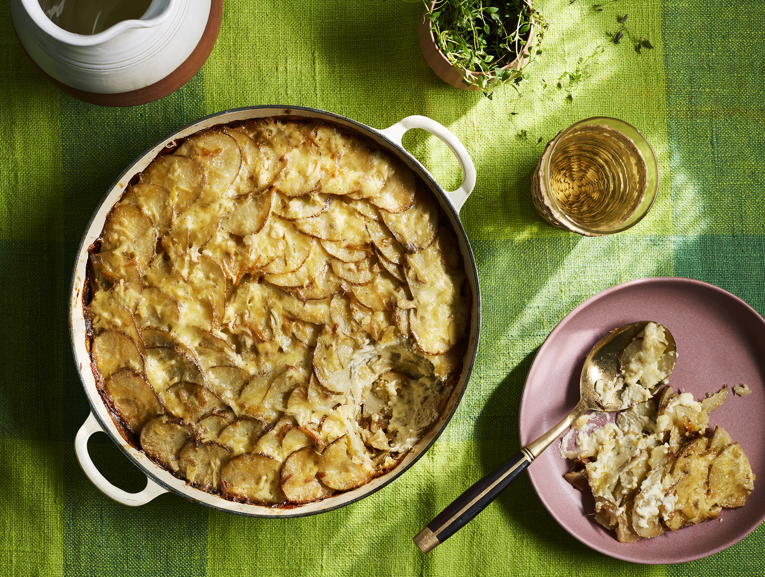 Overhead shot of scalloped potatoes in a pan, alongside a plate with a serving and a spoon, showcasing a warm, inviting food scene.