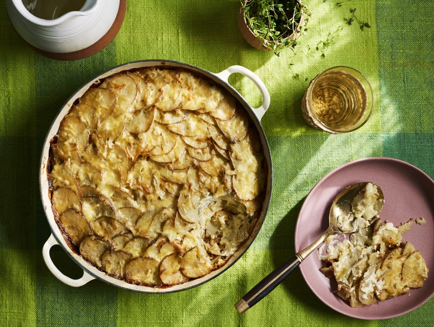 Overhead shot of scalloped potatoes in a pan, alongside a plate with a serving and a spoon, showcasing a warm, inviting food scene.