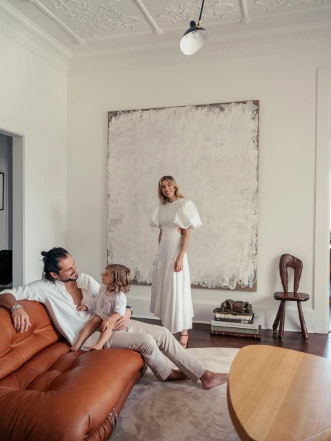 Family portrait in a brightly lit living room. A man and a child are seated on a couch while a woman stands in the background.