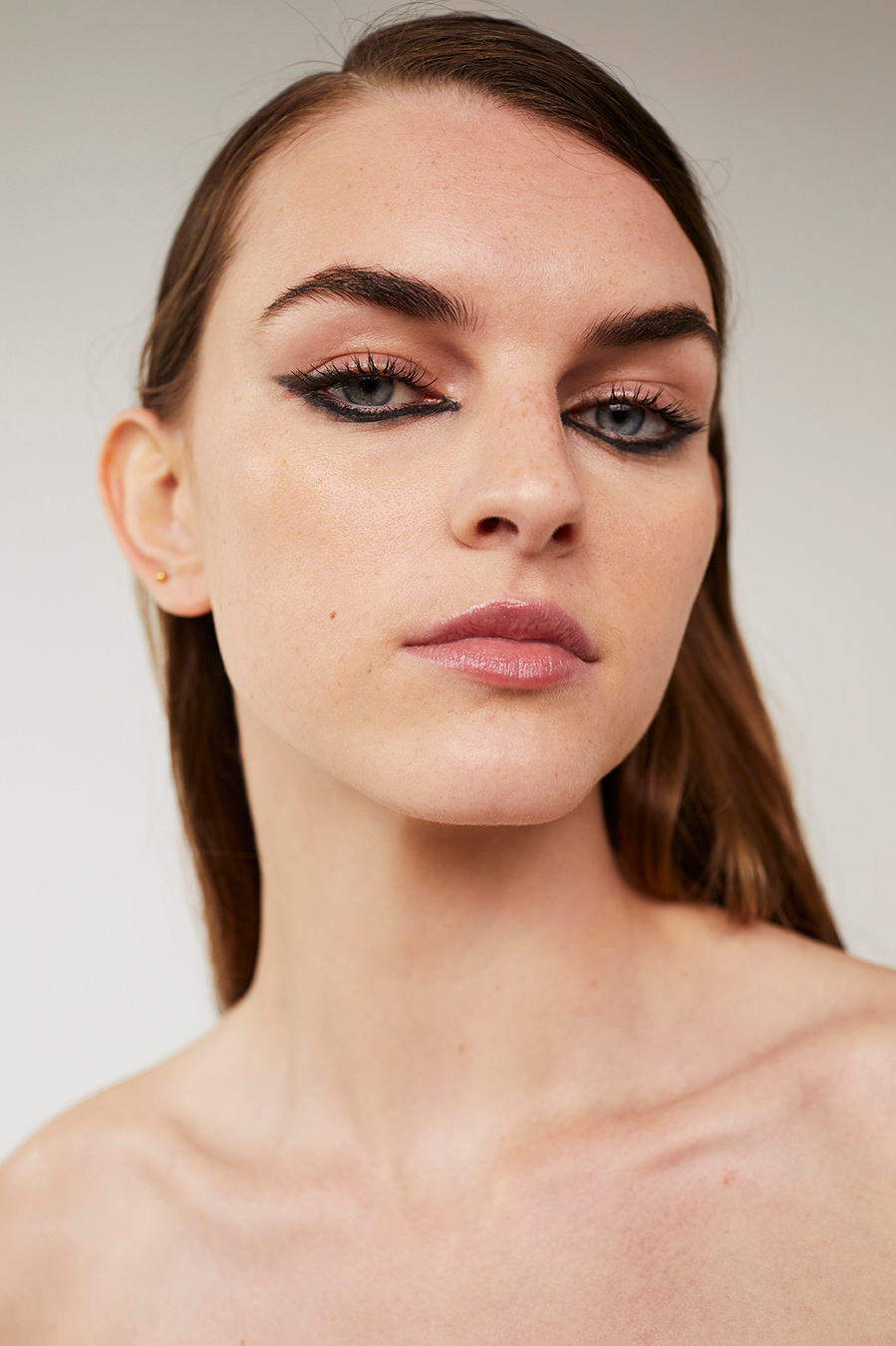 Close-up portrait of an adult woman with brown hair and dramatic black eyeliner makeup posing in front of a neutral background in a photo studio.