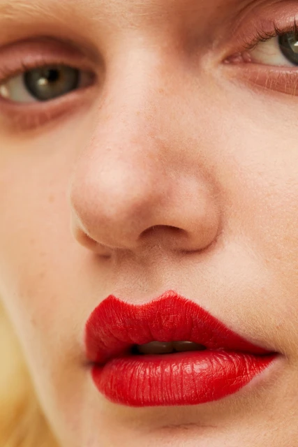 Close-up of a woman's face featuring red lipstick in a heart shape, focusing on the details of her features.