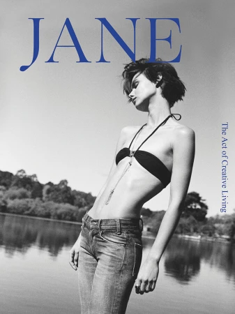 Black and white portrait of a woman wearing a dark bandeau top and jeans outdoors by a body of water