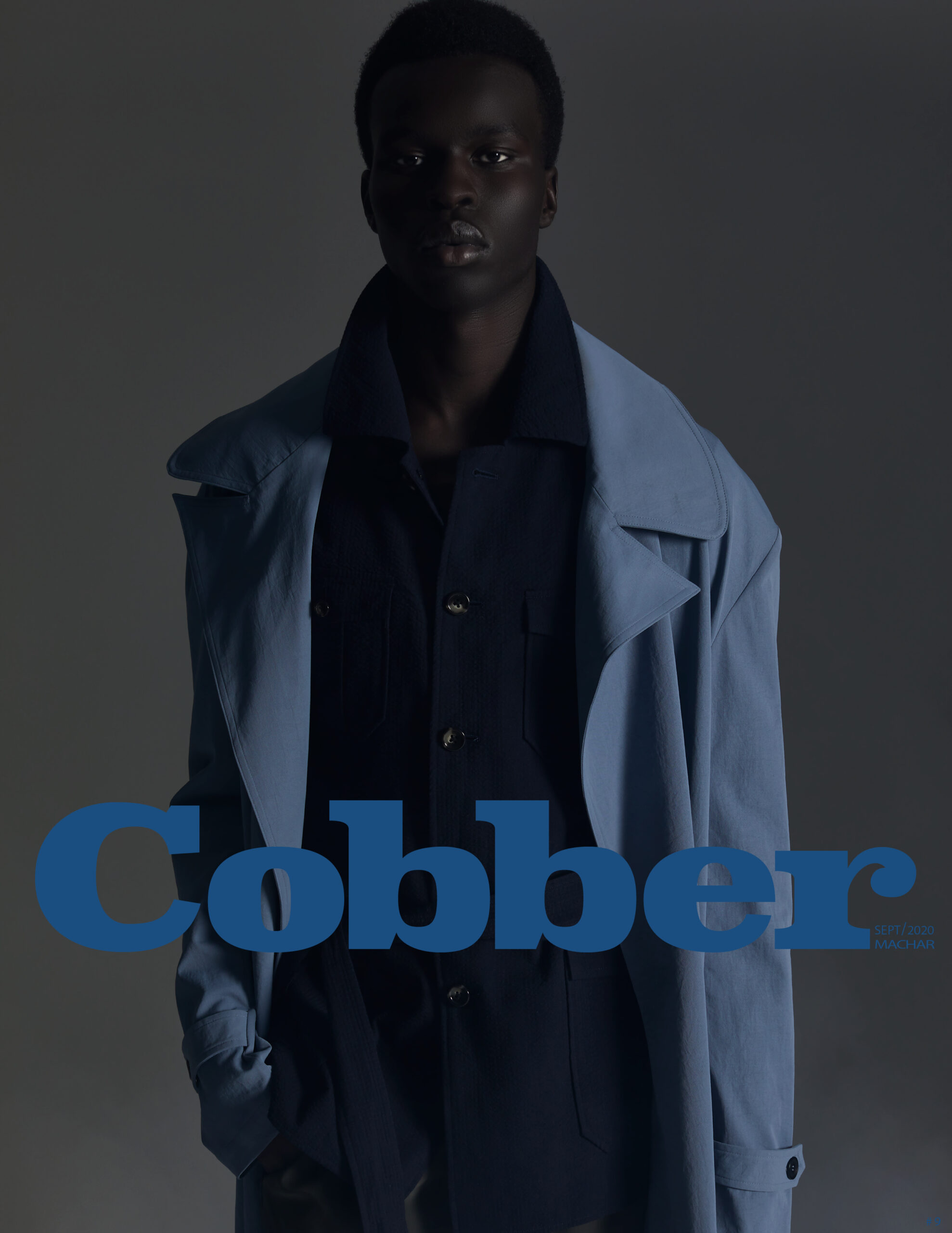 Black male model wearing a light blue coat and dark shirt against a dark grey background with blue text overlay.