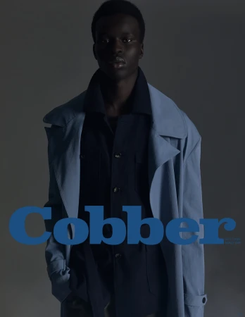 Black male model wearing a light blue coat and dark shirt against a dark grey background with blue text overlay.