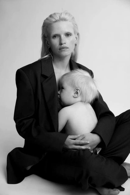 Black and white portrait of a blond woman holding a baby, both sitting on the floor. The woman is wearing a dark suit jacket.