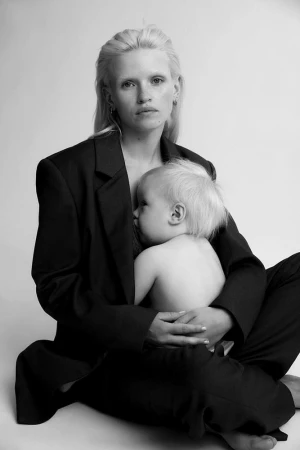 Black and white portrait of a blond woman holding a baby, both sitting on the floor. The woman is wearing a dark suit jacket.