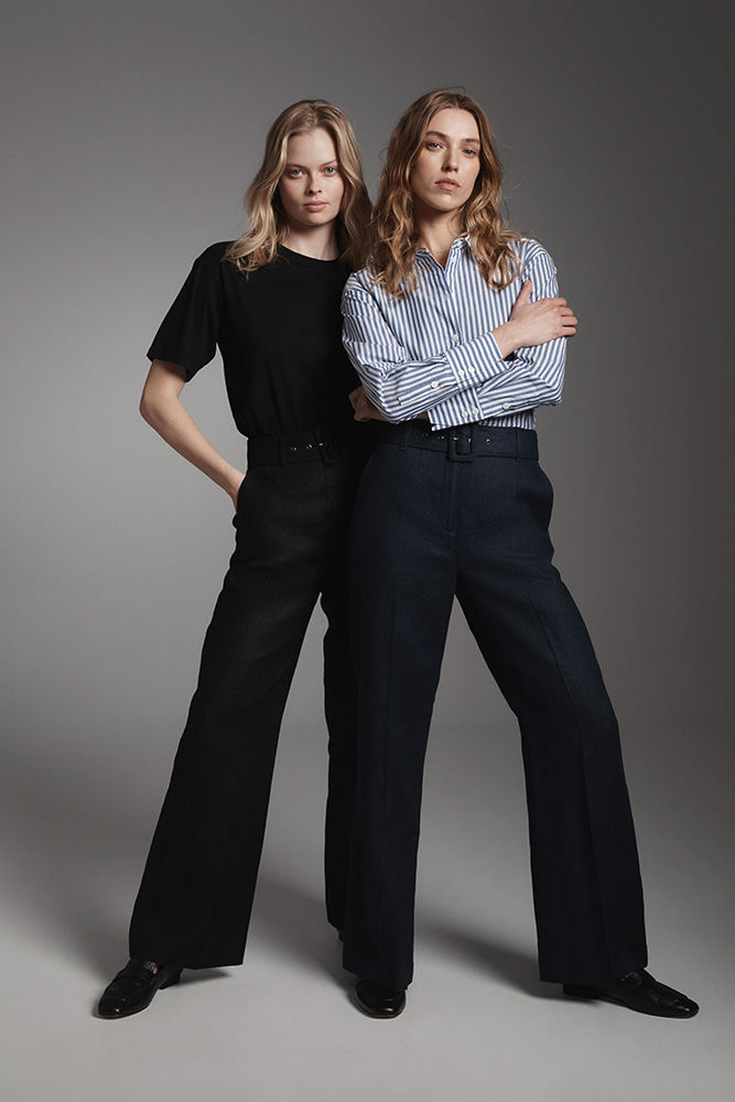 Two female fashion models pose in a studio wearing a short-sleeve t-shirt and a striped long-sleeve shirt, both with wide-leg pants.