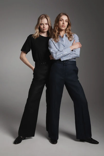 Two female fashion models pose in a studio wearing a short-sleeve t-shirt and a striped long-sleeve shirt, both with wide-leg pants.