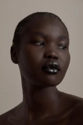 Close-up portrait of a Black woman with glossy metallic dark lips and braided hair against a neutral background