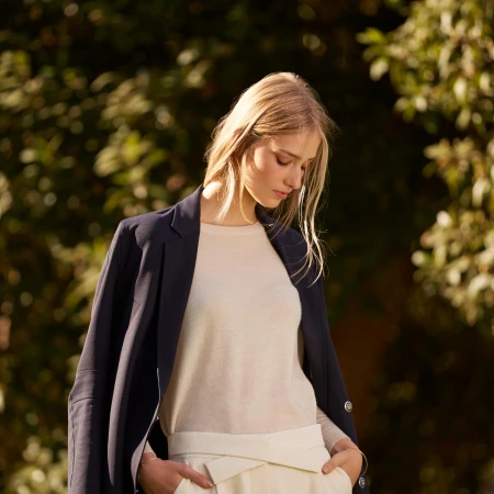Blonde woman wearing a cream top and dark blazer outdoors with her hands in her pockets