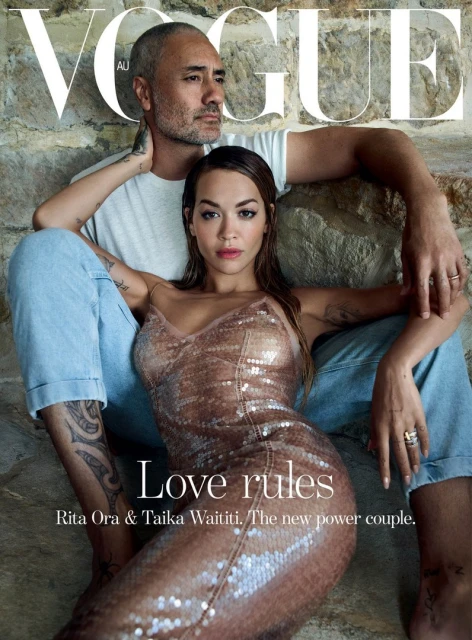 Vogue cover featuring Taika Waititi and Rita Ora posing on stone steps, she's in a gold dress, he's in a white tee and jeans.
