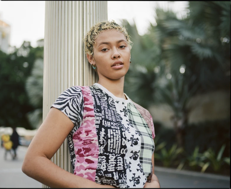 A woman with fair skin and blonde hair poses indoors wearing a black top and jeans, against a neutral backdrop.