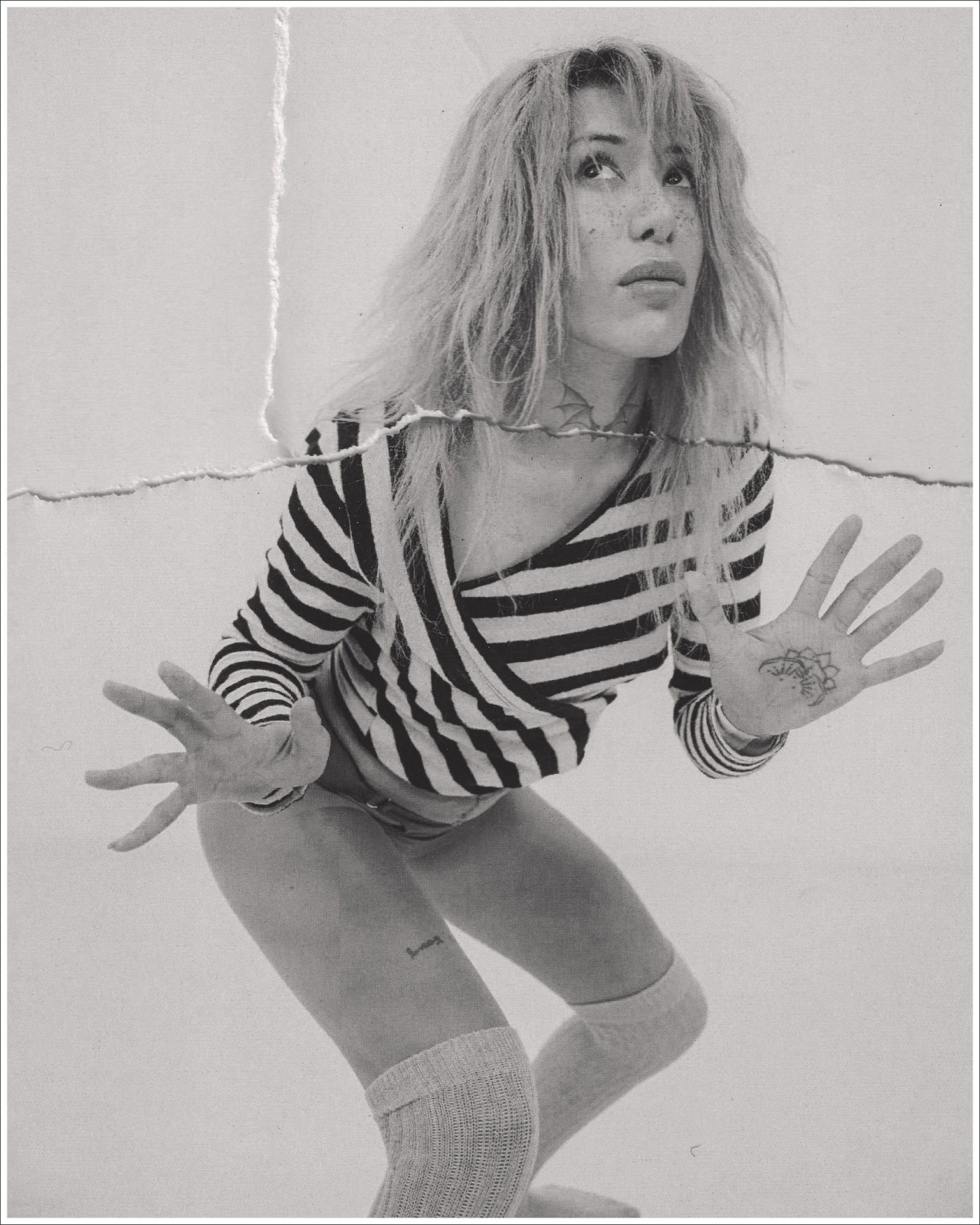 Monochrome portrait of a woman in a striped top and knee-high socks looking upward with hands raised.