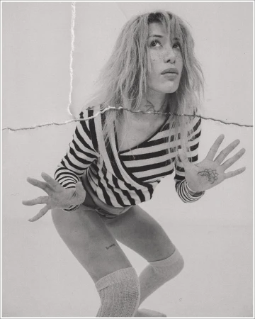 Monochrome portrait of a woman in a striped top and knee-high socks looking upward with hands raised.