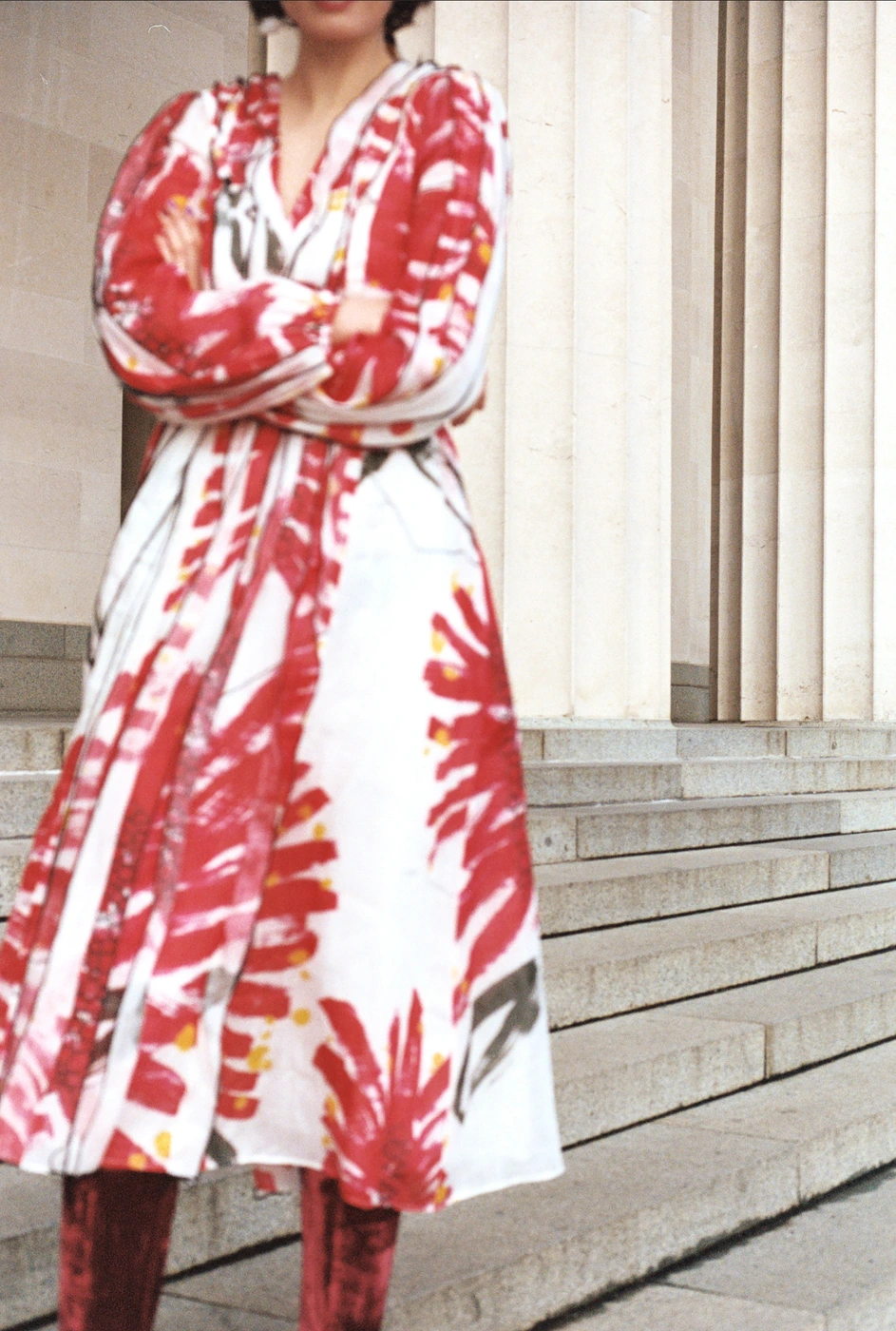 Woman wearing a patterned white and red dress standing on stone steps in front of neoclassical columns