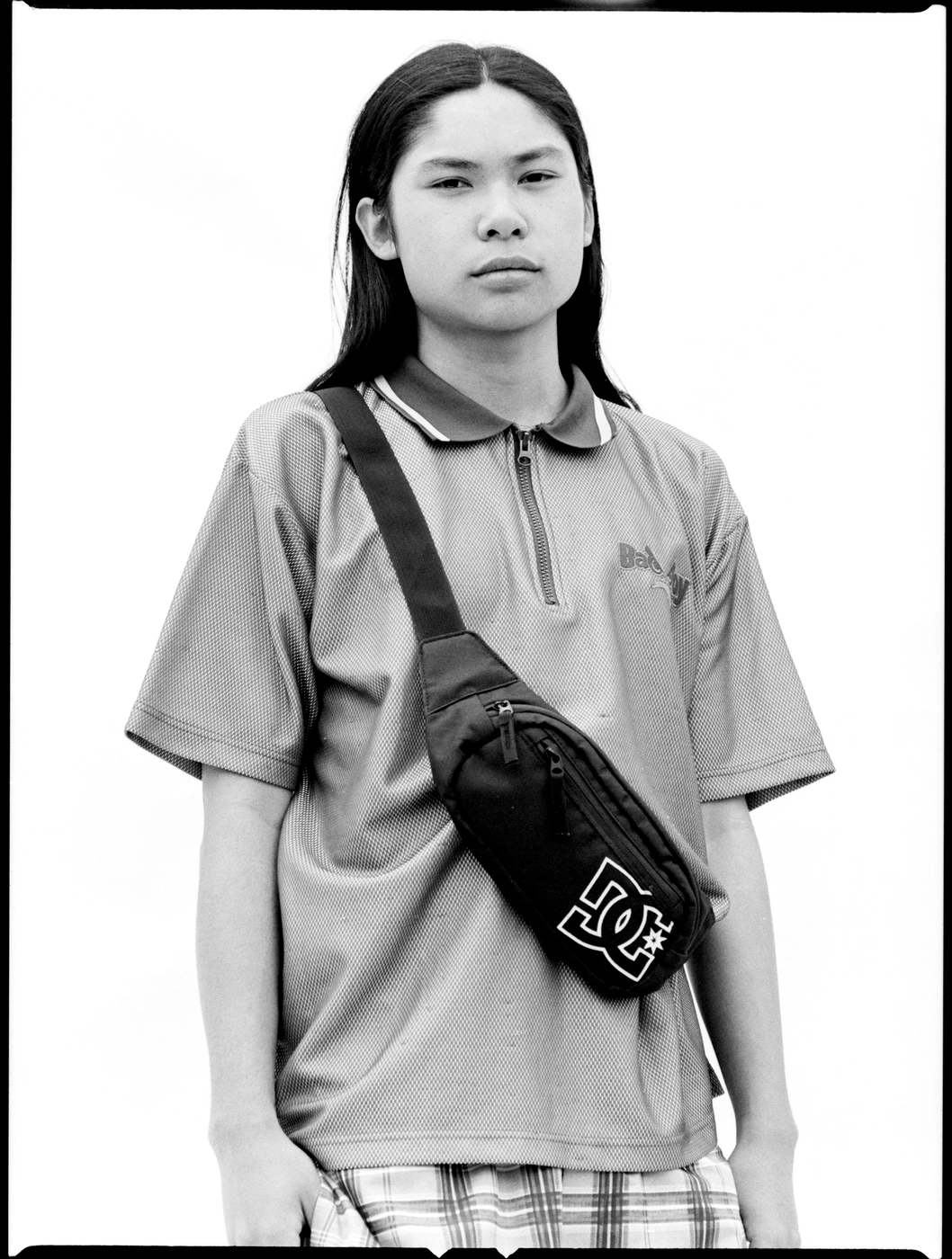Portrait of a person wearing a polo shirt and a crossbody bag against a plain background