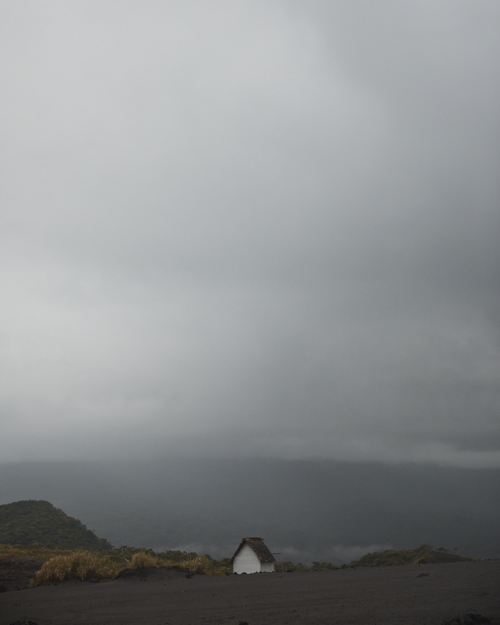 Scenic landscape shot of a small white house in the countryside under an overcast sky with rolling hills in the distance.