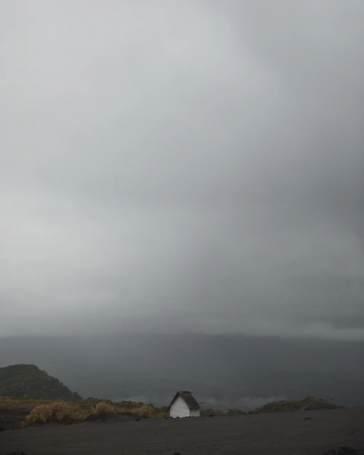 Scenic landscape shot of a small white house in the countryside under an overcast sky with rolling hills in the distance.