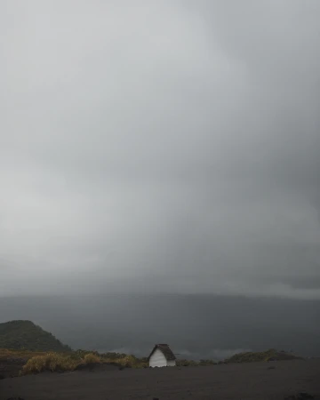 Scenic landscape shot of a small white house in the countryside under an overcast sky with rolling hills in the distance.