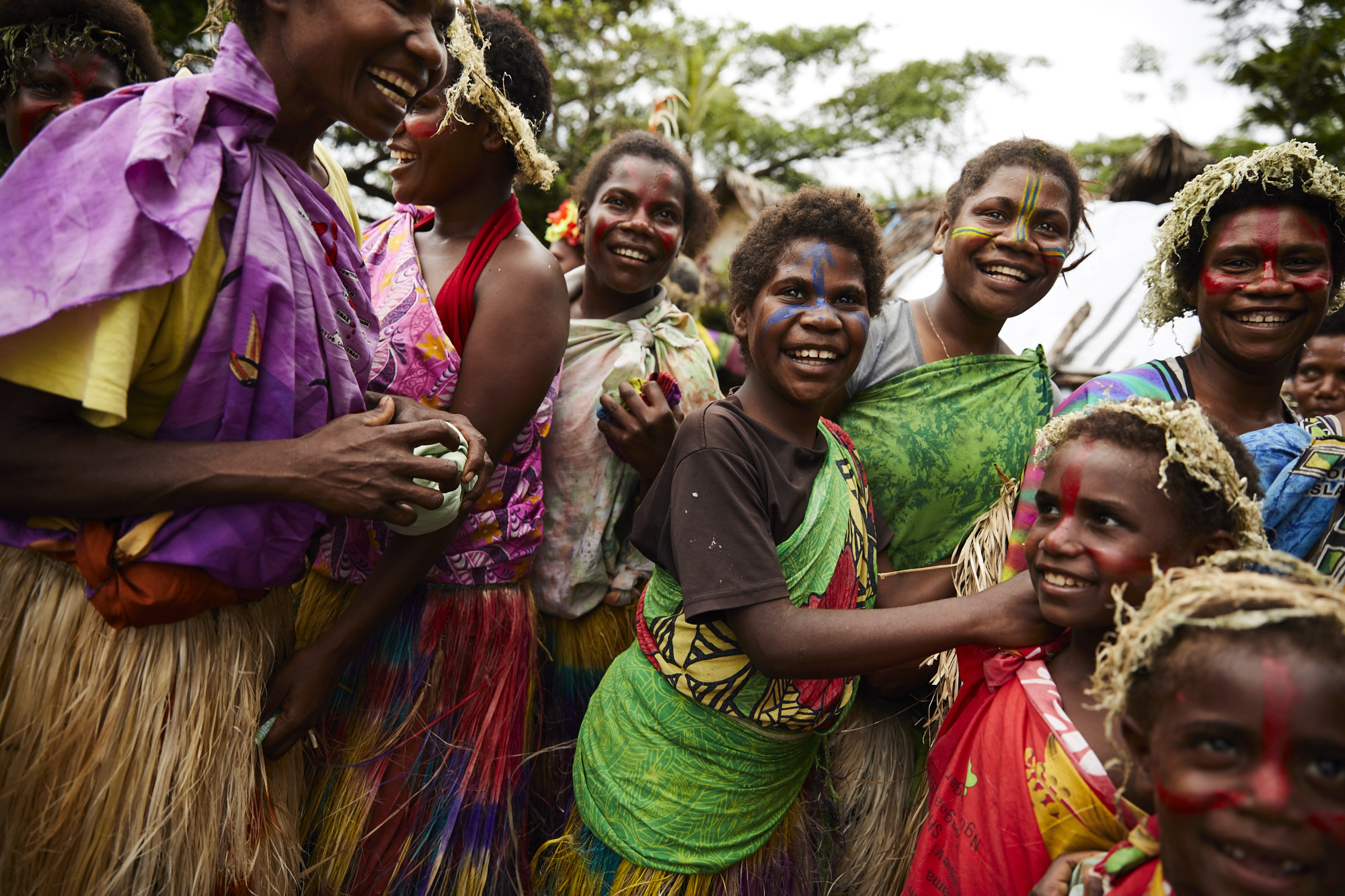 Group of smiling indigenous people with face paint and traditional clothing in an outdoor setting, showcasing cultural celebration and unity.
