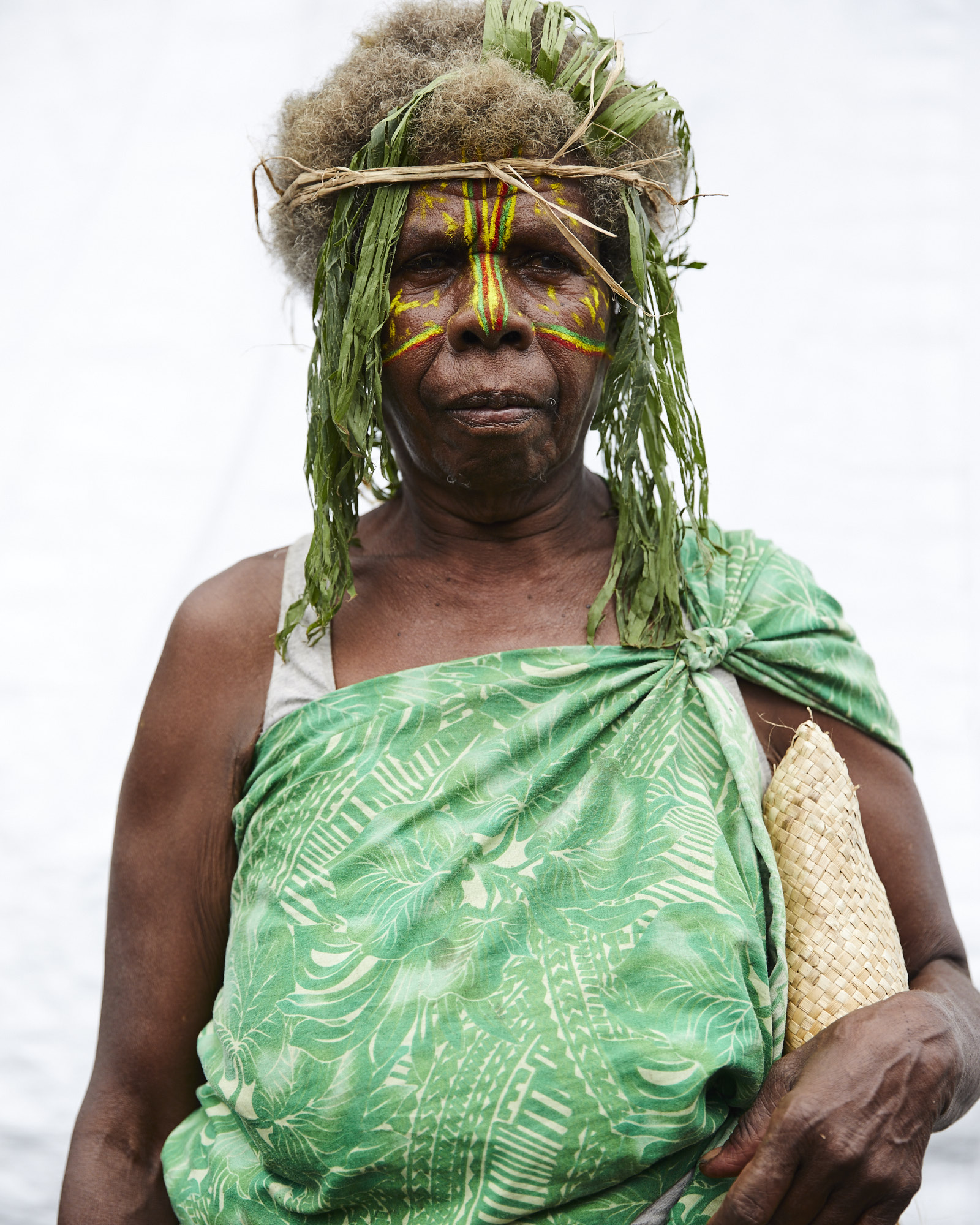 Portrait of an indigenous woman with face paint, a leaf headdress, and a green patterned cloth draped over her shoulder.
