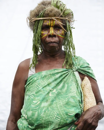 Portrait of an indigenous woman with face paint, a leaf headdress, and a green patterned cloth draped over her shoulder.