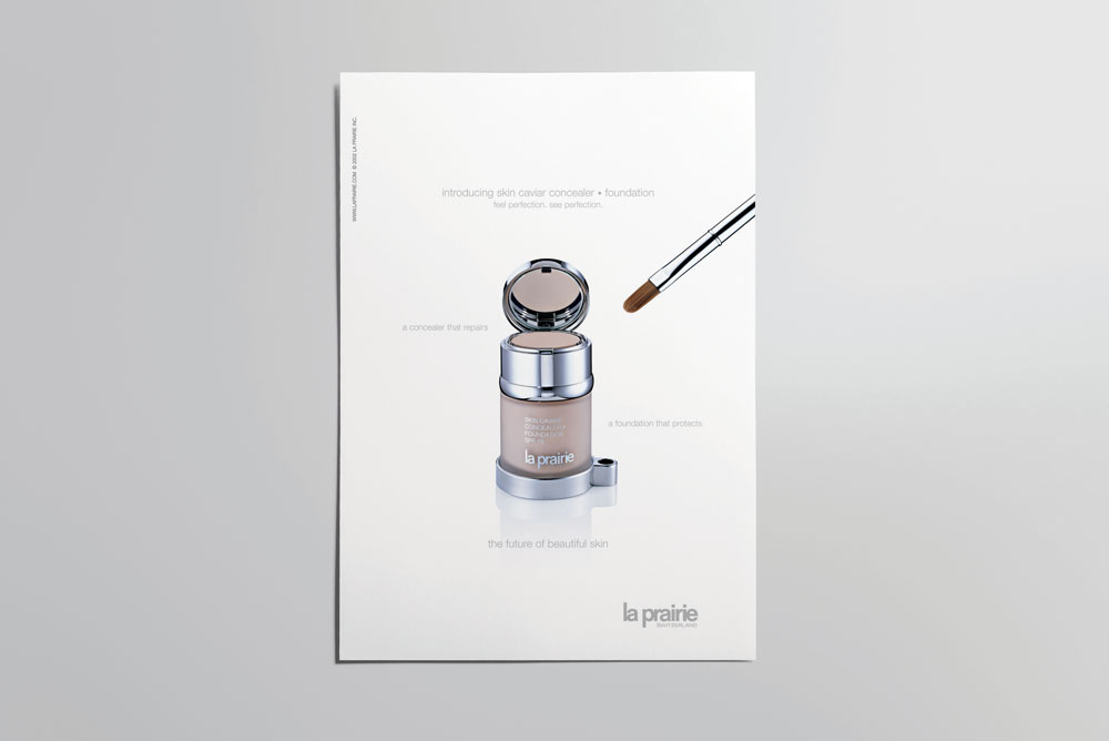 La Prairie skin caviar concealer and foundation product shot on white, accompanied by a silver makeup brush in a studio setting.