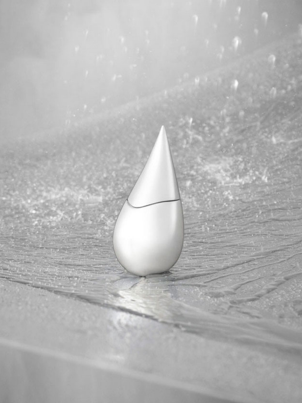 Product shot of a silver perfume bottle on a wet stone surface with a blurry background of water droplets for a clean, fresh aesthetic.