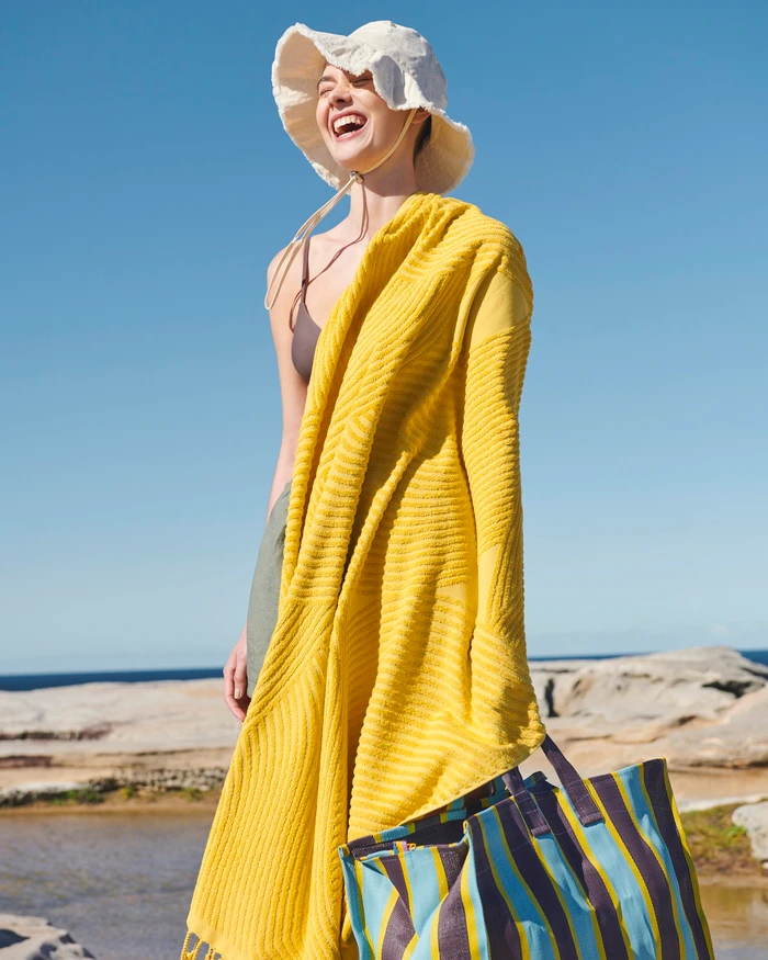 Laughing woman wearing a sun hat and yellow towel by the coast under clear blue sky