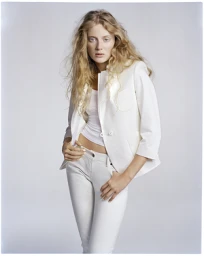 Portrait of a blonde woman in a white jacket and pants standing against a pale seamless background