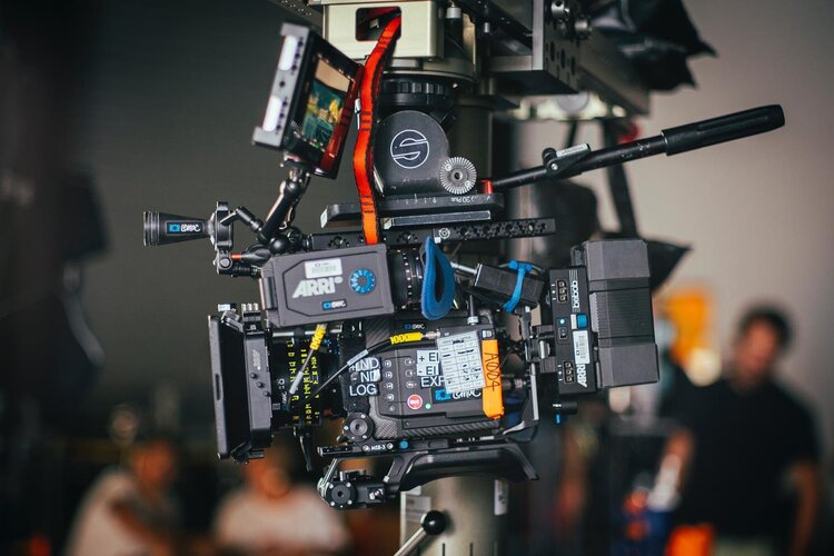 Professional Arri cinema camera on a tripod in a studio setting, showcasing advanced film equipment with blurry figures in the background.