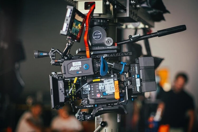 Professional Arri cinema camera on a tripod in a studio setting, showcasing advanced film equipment with blurry figures in the background.